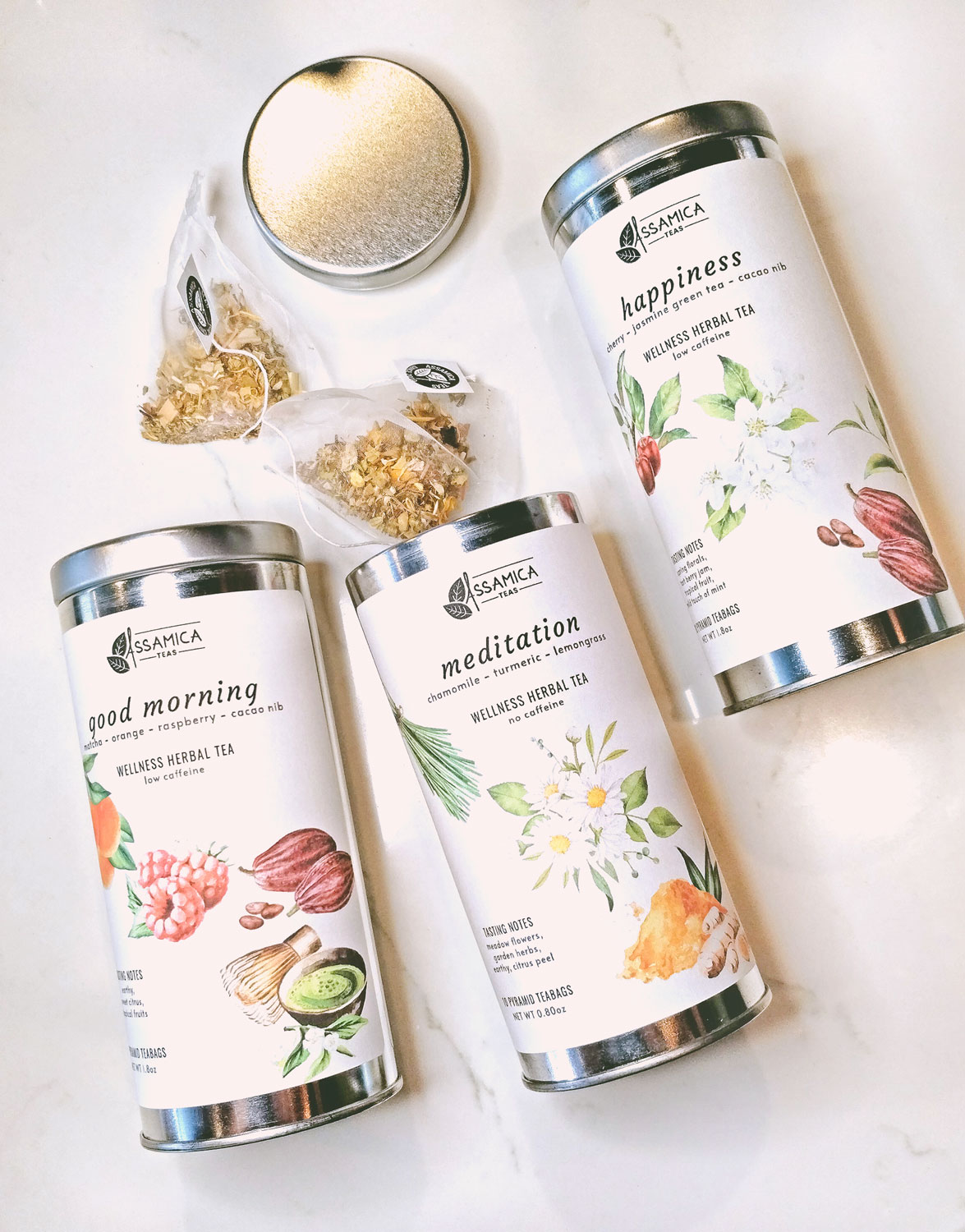 3 Wellness Teas in long tin containers, with 2 pyramid teabags spilling out of one container.